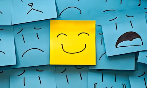 Post-its azuis com expressões tristes, preocupadas e desanimadas, destacando no centro um post-it amarelo com um rosto sorridente e feliz, simbolizando organização, clareza e leveza em meio ao caos. Representa como a organização nos projetos de vídeo traz mais tranquilidade e produtividade.