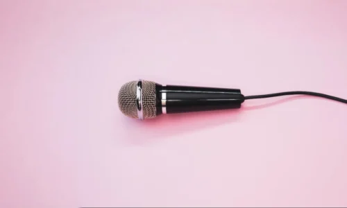 Microfone dinâmico com acabamento metálico e cabo preto sobre fundo rosa suave, representando simplicidade na comunicação